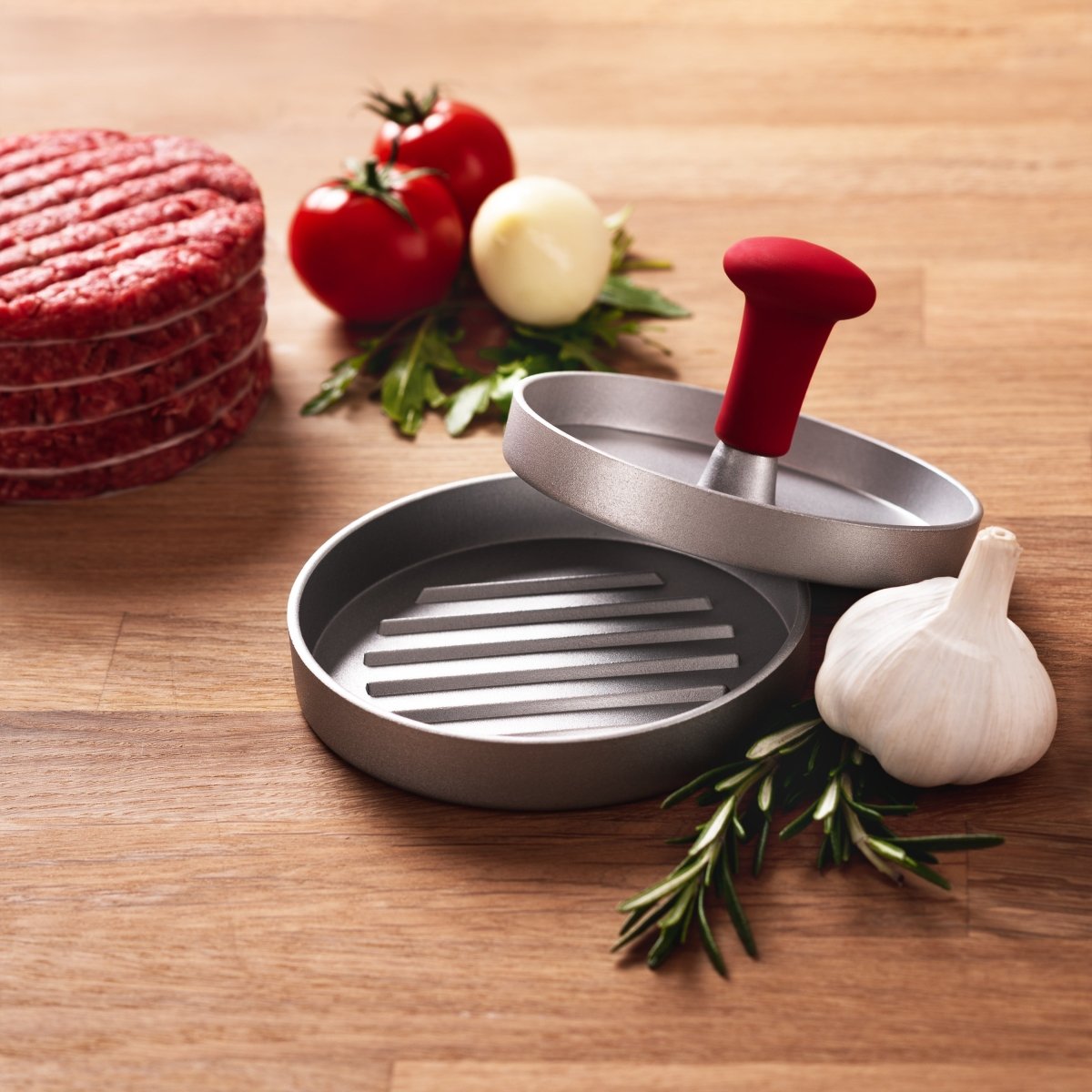 Burgerpresse mit rotem Stempel auf einer Holzoberfläche neben Zutaten und einem Stapel Burgerpatties.