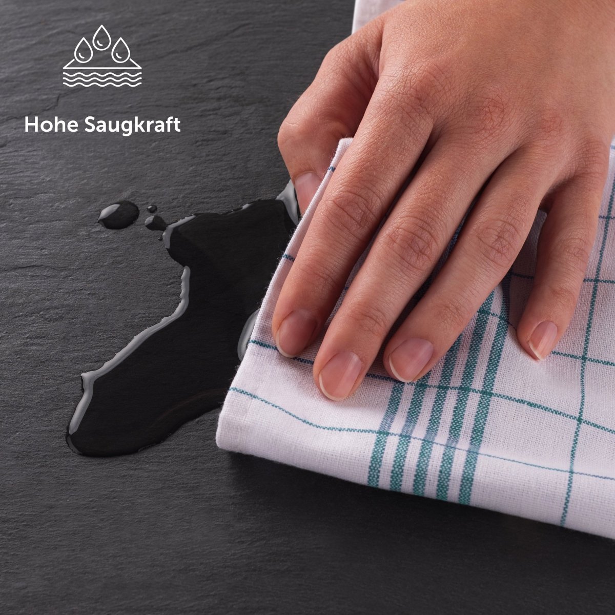 Hand wisch eine Flüssigkeit auf einer Schieferplatte mit einem Geschirrtuch auf.