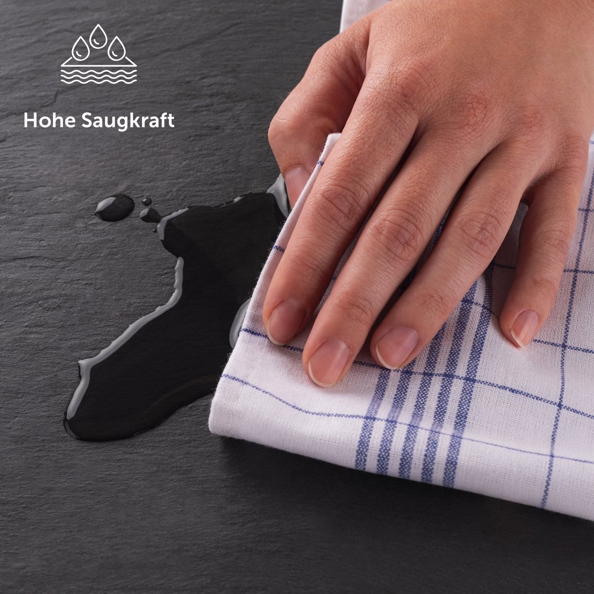 Hand wisch eine Flüssigkeit auf einer Schieferplatte mit einem Geschirrtuch auf.