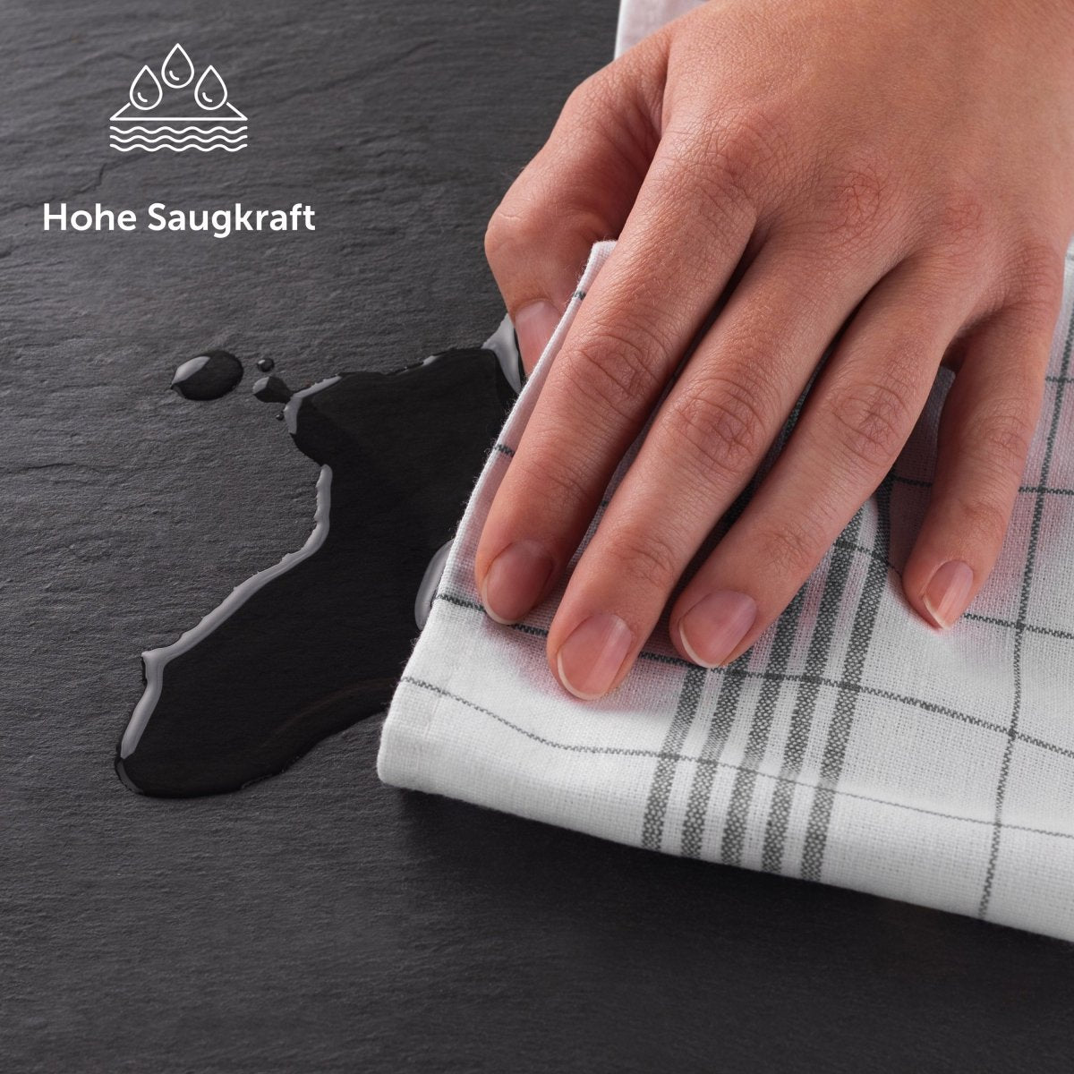 Hand wisch eine Flüssigkeit auf einer Schieferplatte mit einem Geschirrtuch auf.