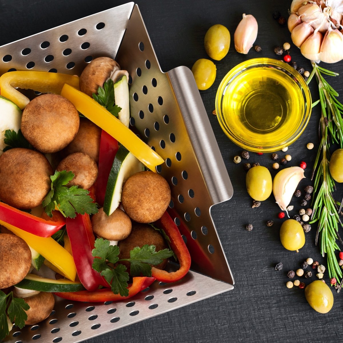 Kleiner Edelstahl-Grillkorb mit Gemüse und Pilzen auf einer Grillfläche.