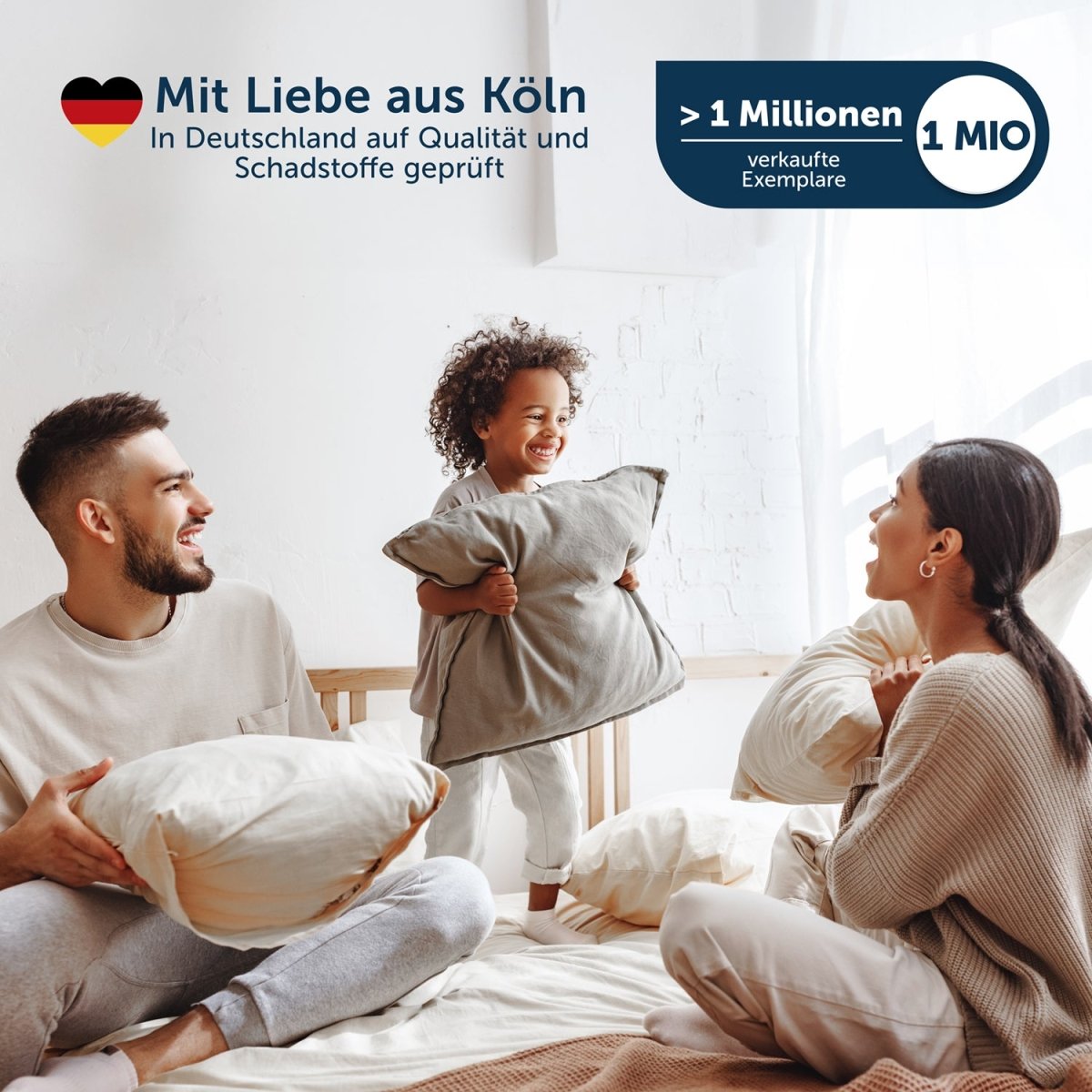 Familie mit zwei Erwachsenen und einem Kind, die auf einem Bett mit weißen Kissen spielen.