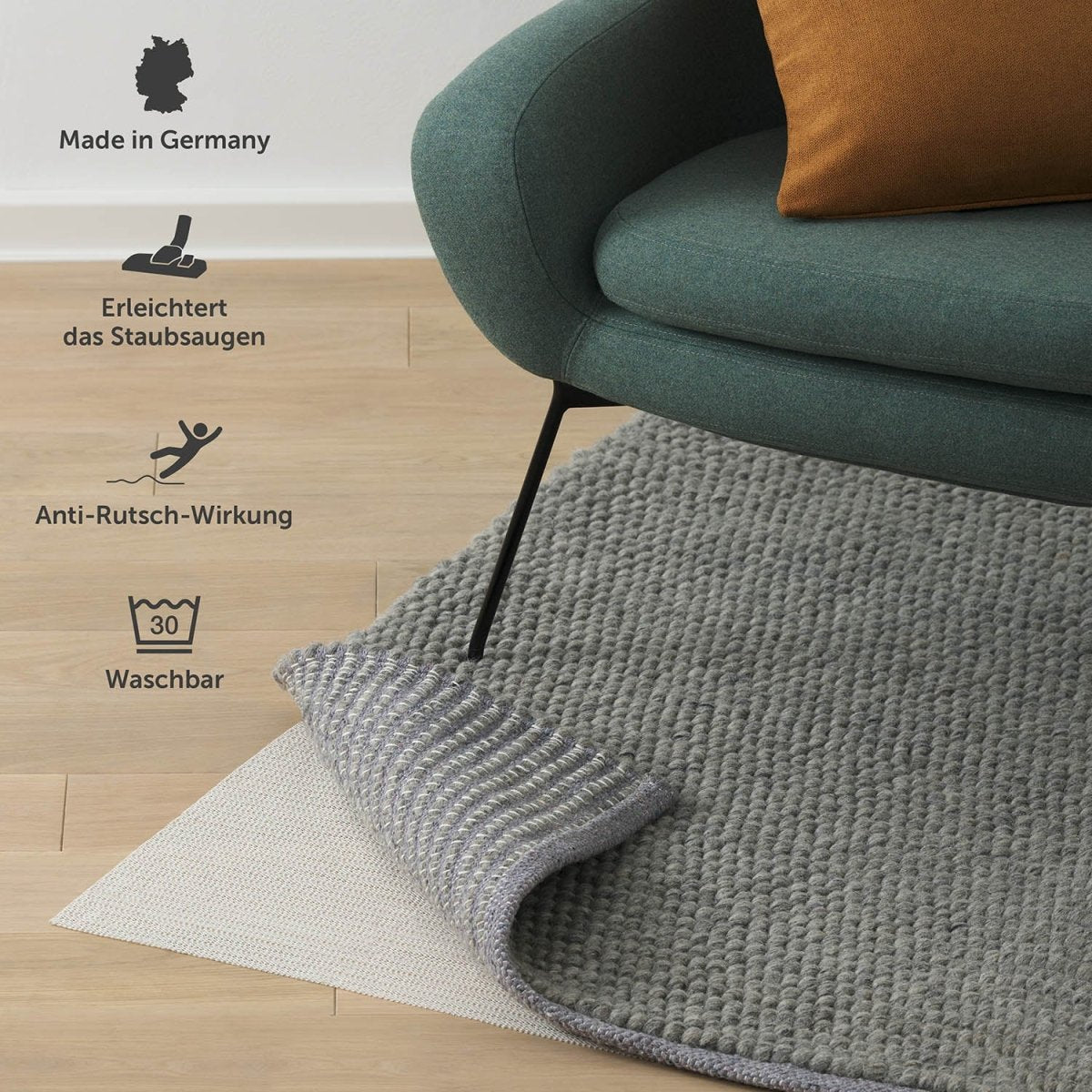 Eine Antirutschmatte unter einem grauen Teppich auf Holzboden, "Made in Germany", waschbar bei 30 Grad und mit Anti-Rutsch-Wirkung, die das Staubsaugen erleichtert.