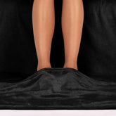 Nahaufnahme von zwei barfüßigen Beinen die auf einem schwarz flauschigen Stoff stehen.