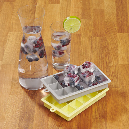 Zwei Getränkegläser mit Eiswürfeln neben grauer und gelber Eiswürfelform auf Holztisch.