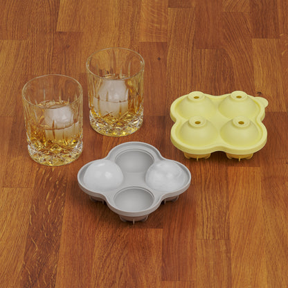 Zwei Whiskygläser mit Eiskugeln neben einer leeren und einer vollen grauen Eiskugelform auf Holzoberfläche.