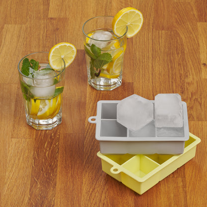 Zwei Getränkegläser mit Eiswürfeln neben grauer und gelber Eiswürfelform auf Holztisch.