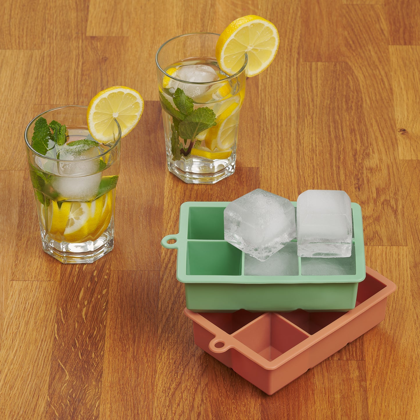 Getränkegläser mit Eiswürfeln neben leerer und voller roter Eiswürfelform auf Holztisch.