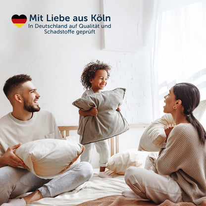 Eine glückliche Familie auf einem Bett wobei die Qualität und Schadstofffreiheit des Produkts mit 'Mit Liebe aus Köln' unterstrichen wird.