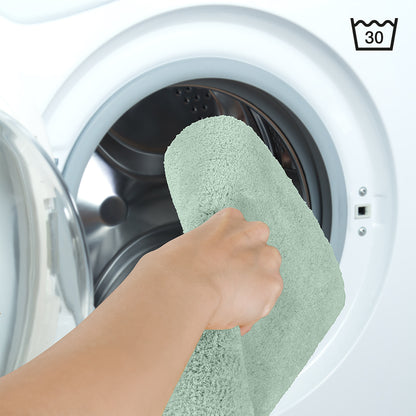 Badezimmerteppich wird in eine Waschmaschine gelegt mit Wäschesymbol für 30 Grad.