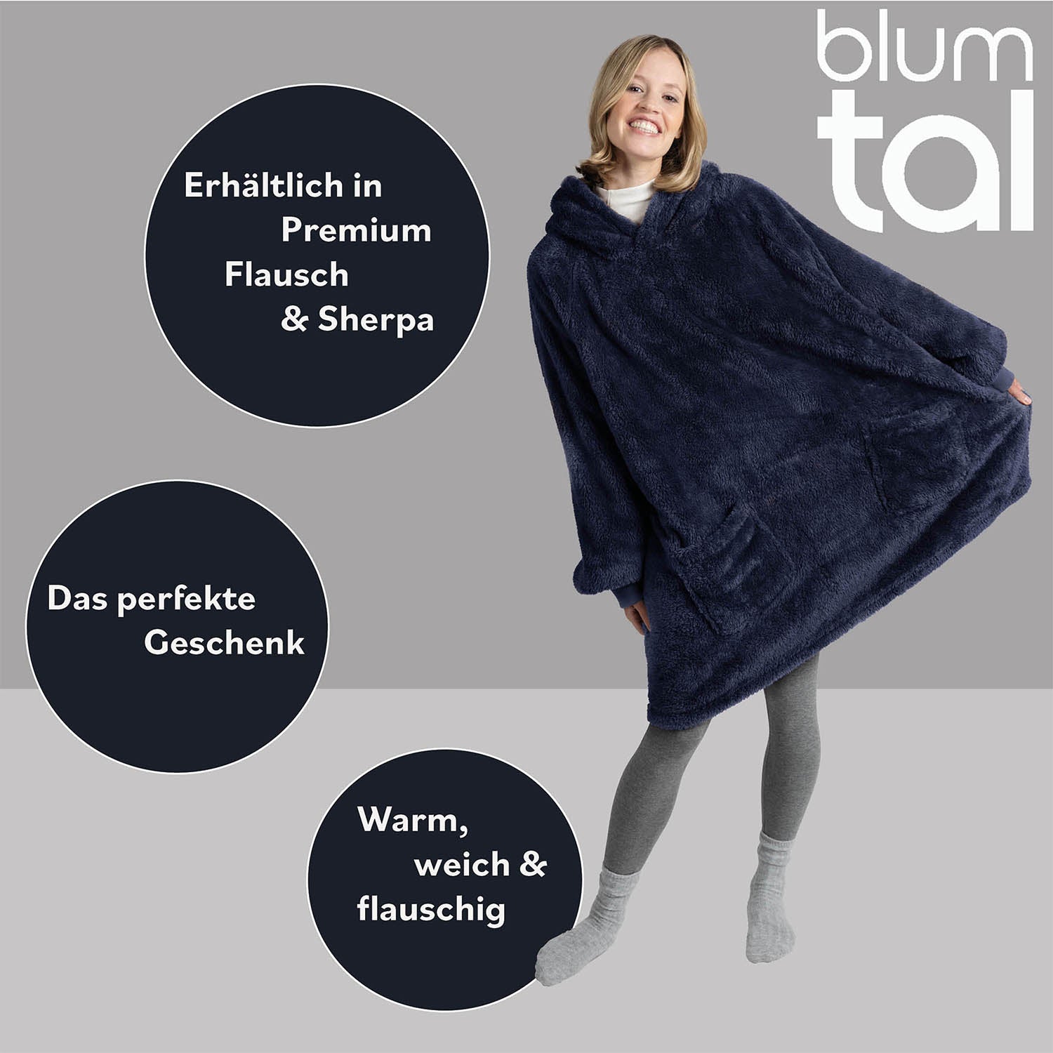 Lächelnde Frau in grauer Leggings zeigt eine blaue Oversize-Kuscheljacke, Textelemente betonen Verfügbarkeit in Premium Flausch &amp; Sherpa und als ideales Geschenk.