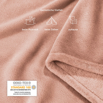 Detailansicht der rosafarbenen Fleece-Kuscheldecke mit Piktogrammen, die vielfältige Einsatzmöglichkeiten wie beim Picknick, Zelten und zu Hause zeigen, inklusive OEKO-TEX Standard 100 Siegel.