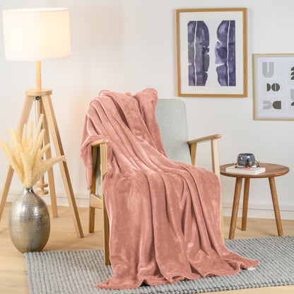 Rosafarbene Fleece-Kuscheldecke stilvoll über einen hellen Sessel in einem modern eingerichteten Wohnzimmer drapiert, mit einem Beistelltisch und einer Vase daneben.