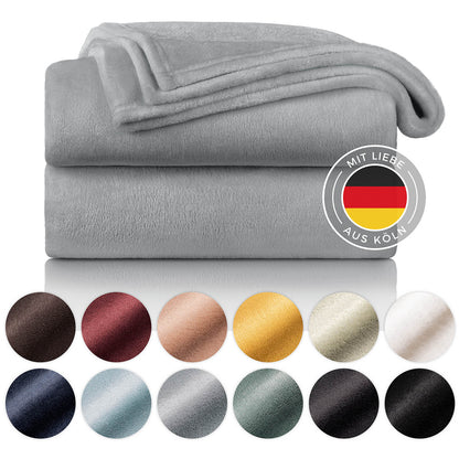 Gestapelte graue Fleecedecken mit Farbmusterpalette und dem Siegel 'Mit Liebe aus Köln' auf weißem Hintergrund.
