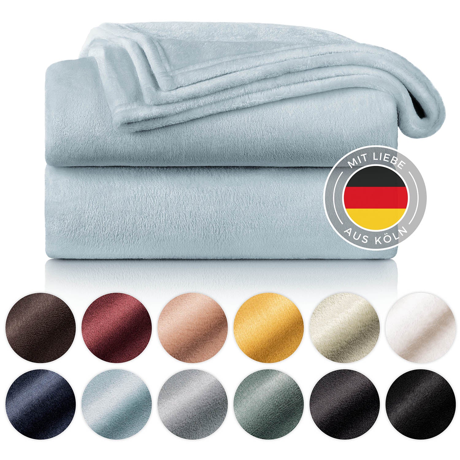Gestapelte hellblaue Fleece-Kuscheldecken mit einem Label 'Mit Liebe aus Köln' und einer Farbauswahl darunter.