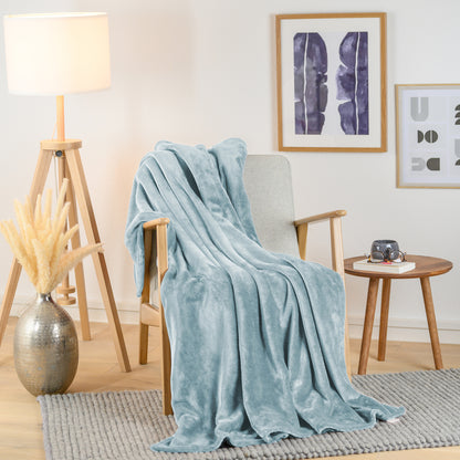 Hellblaue Fleece-Kuscheldecke stilvoll über einen hellen Sessel in einem modern eingerichteten Wohnzimmer drapiert, mit einem Beistelltisch und einer Vase daneben.