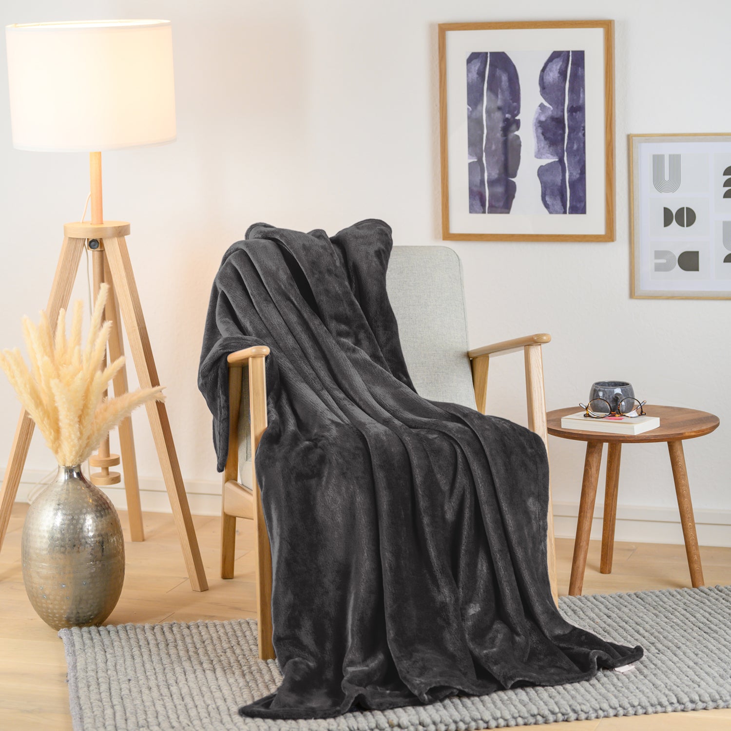 Schwarze Fleecedecke über einen Sessel in einem stilvoll eingerichteten Wohnzimmer geworfen, mit dekorativer Vase und Bild im Hintergrund.