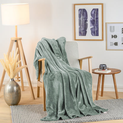 Salbeigrüne Fleece-Kuscheldecke stilvoll über einen hellen Sessel in einem Wohnzimmer drapiert, mit Beistelltisch und Dekoration.