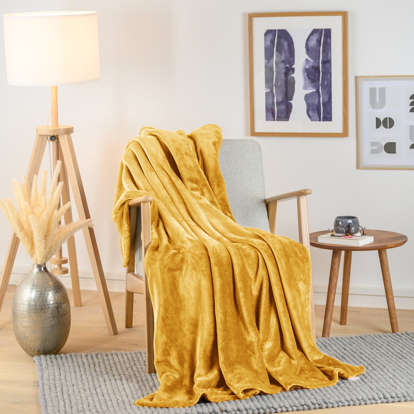 Senfgelbe Fleece-Kuscheldecke elegant drapiert über einen Sessel in einem stilvollen Wohnraum, neben einer Stehlampe und Pflanzendekoration.
