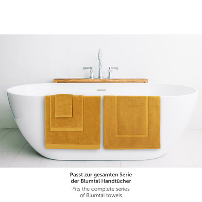 Gelbes Handtuch neben Badewanne passend zur Blumtal Handtuchserie.