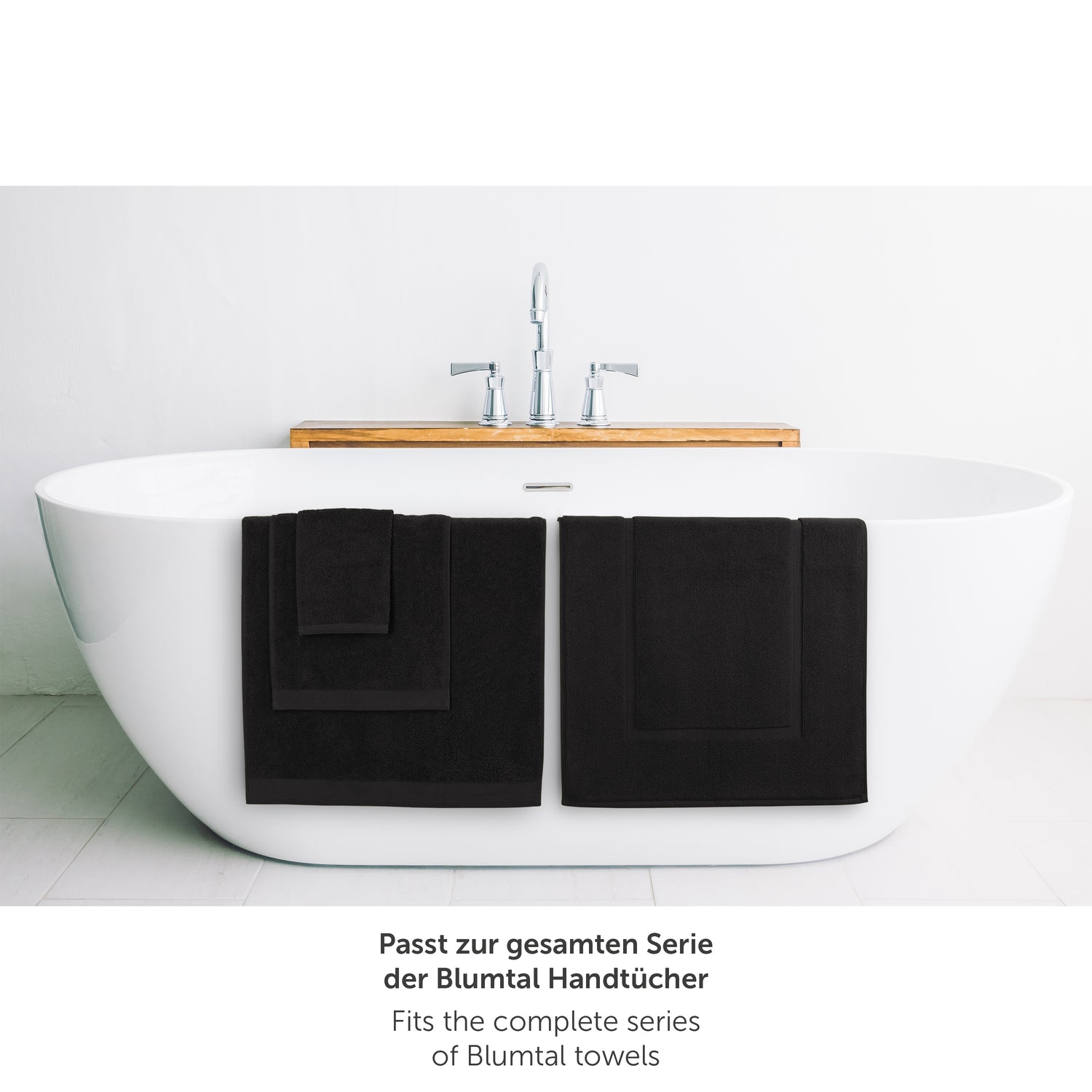 Schwarzes Handtuch neben Badewanne passend zur Blumtal Handtuchserie.