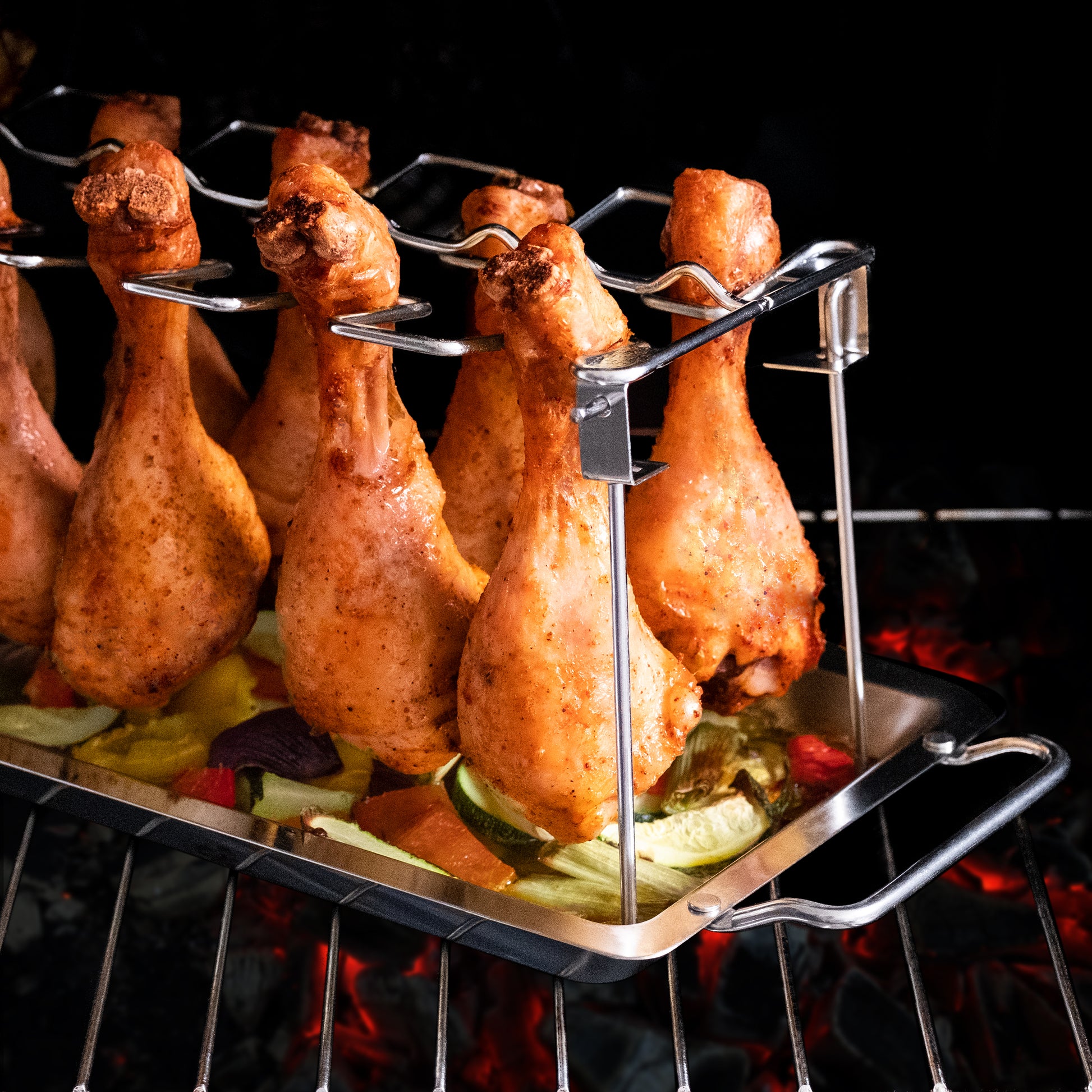 Hühnerbeine auf einem Ständer, der auf einem Grill über glühender Kohle steht, mit Gemüse darunter.