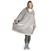 Frau in grauer Leggings und Socken lächelt, während sie eine graue Sherpa-Kuscheljacke mit weißen Saumdetails und großen Taschen trägt.