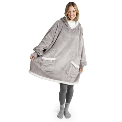 Frau in grauer Leggings und Socken lächelt, während sie eine graue Sherpa-Kuscheljacke mit weißen Saumdetails und großen Taschen trägt.