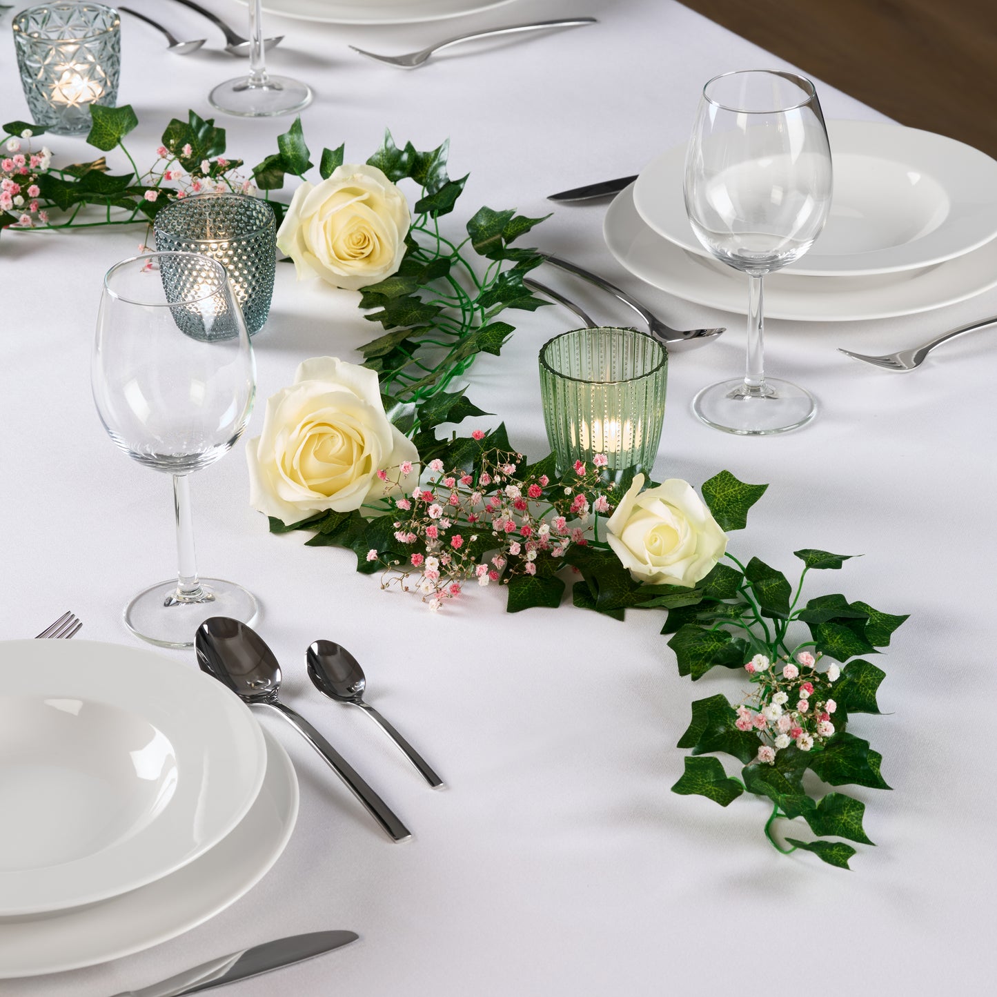 Tischdekoration mit grünen Pflanzen und weißen Rosen für ein Dinner-Setting.