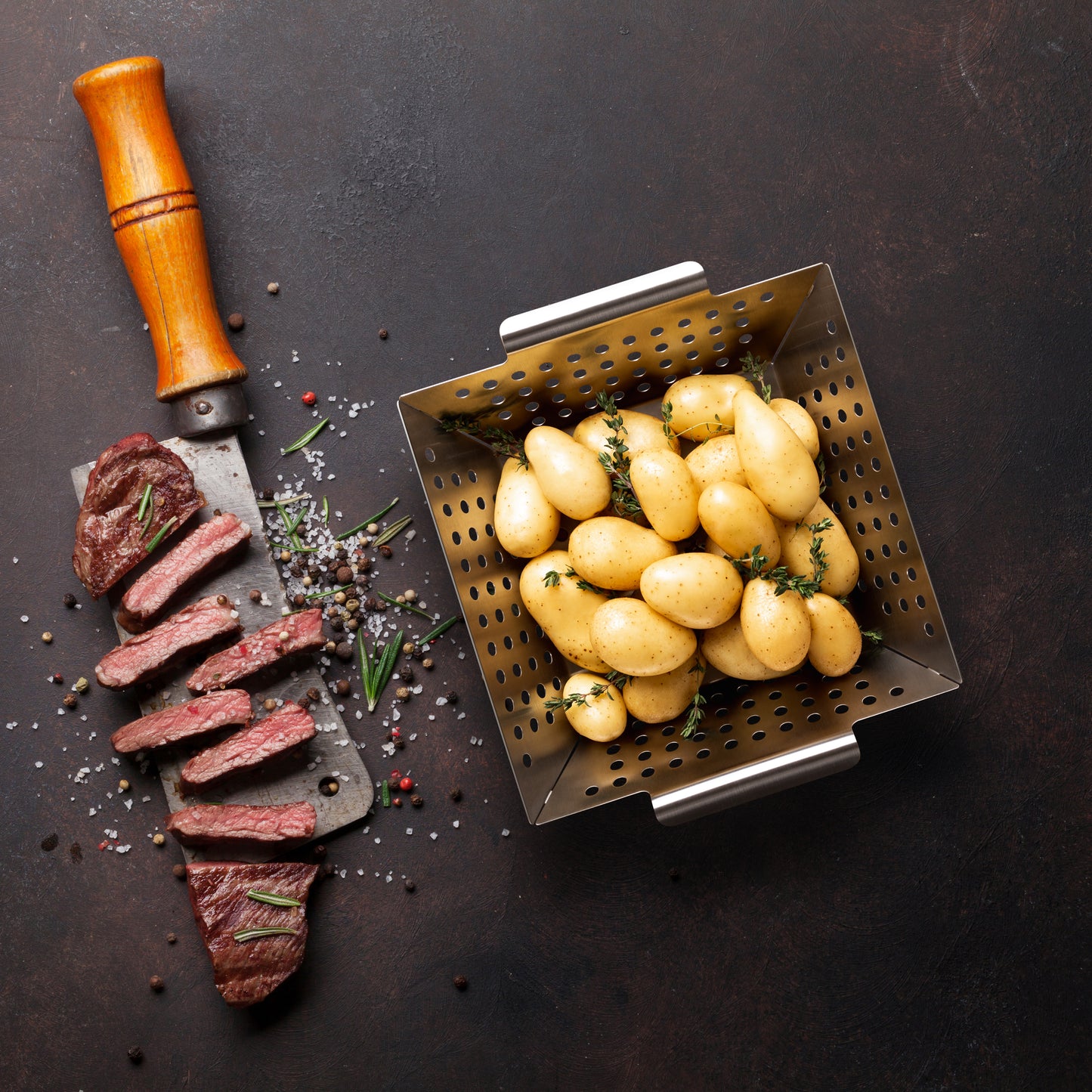 Kleiner Edelstahl-Grillkorb mit Kartoffeln und Steak auf dunklem Untergrund.