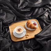 Eine marineblaue Fleece-Kuscheldecke auf einem Bett, mit einem Serviertablett, das ein Frühstück mit Kaffee und Croissant präsentiert, und der Beschreibung &