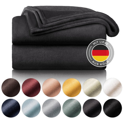 Gestapelte schwarze Fleecedecken mit Farbmusterpalette und dem Siegel &