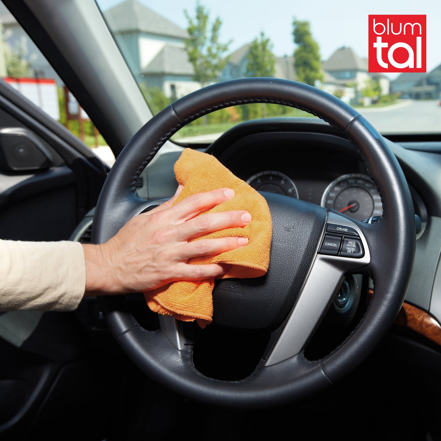 Ein Mikrofasertuch in der Hand einer Person die das Lenkrad eines Autos reinigt.