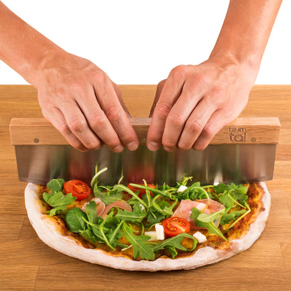 Zwei Hände benutzen das Wiegemesser zum Schneiden der Pizza.