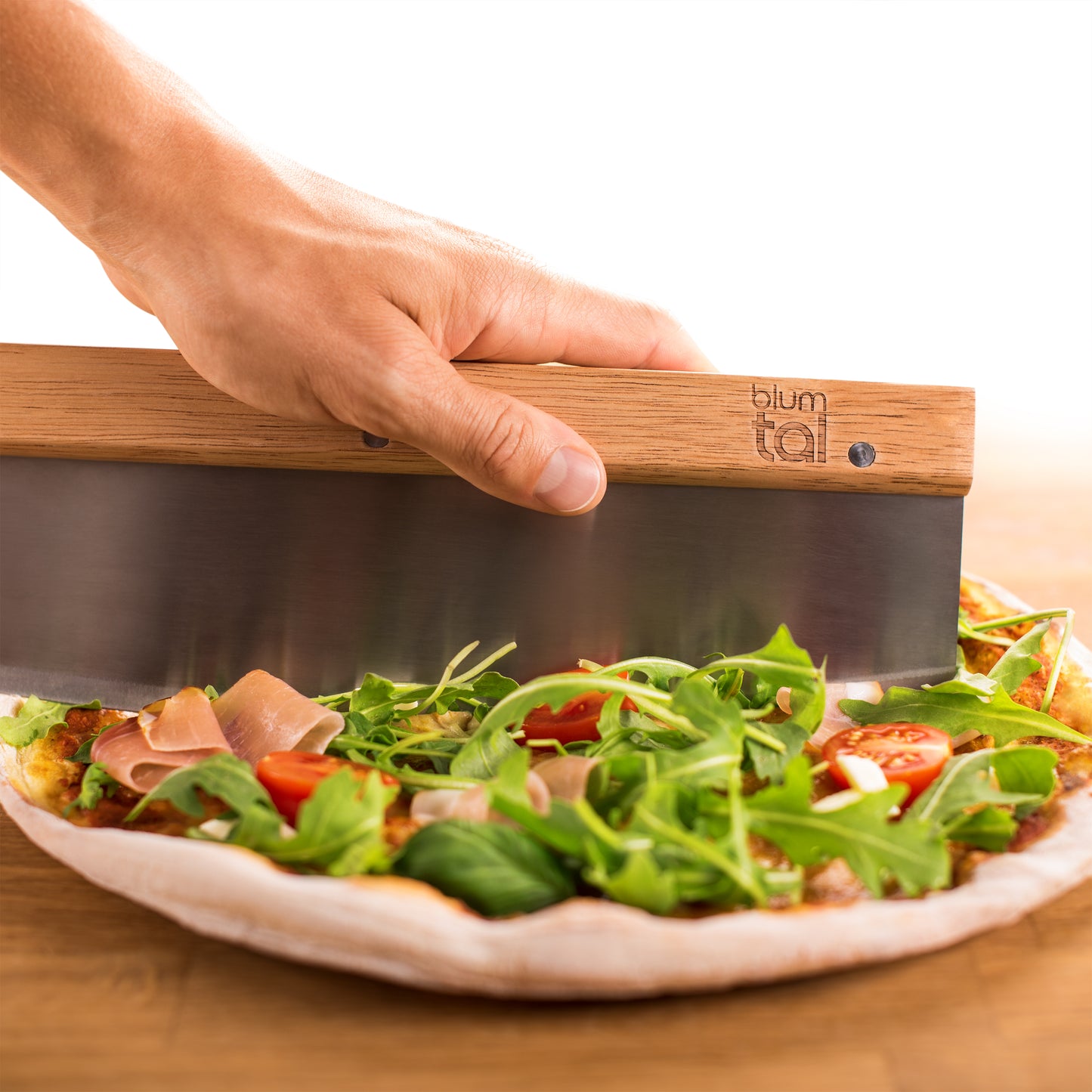 Eine Hand hält das Wiegemesser beim Schneiden der Pizza.