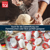 Eine Person bearbeitet einen Brotteig mit Mehl. Darunter ein Flammkuchen mit frischem Belag. Text: „Auch für die Zubereitung von Flammkuchen oder Brot perfekt geeignet. Mit Liebe aus Köln.“