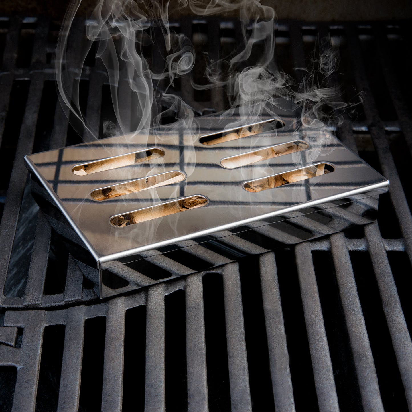 Rauch steigt aus den Schlitzen einer Räucherbox auf einem Grillrost auf.