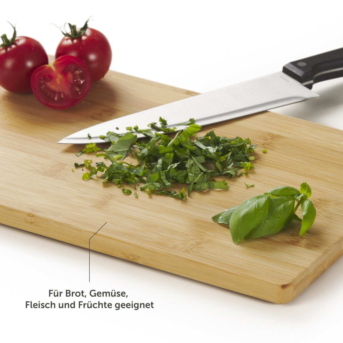 Bambusschneidebrett mit gehackten Kräutern und Tomaten, Hinweis darauf, dass es für Brot, Gemüse, Fleisch und Früchte geeignet ist.