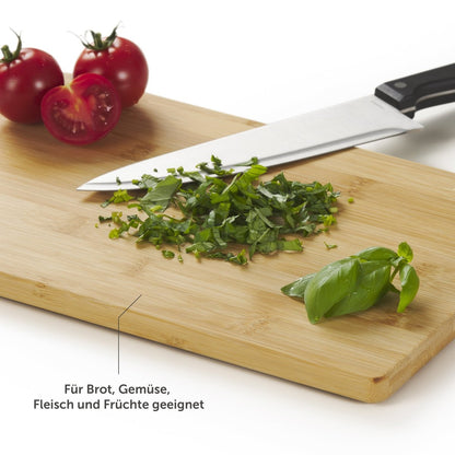 Bambusschneidebrett mit gehackten Kräutern und Tomaten, Hinweis darauf, dass es für Brot, Gemüse, Fleisch und Früchte geeignet ist.