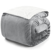 Zusammengerollte graue Decke mit weißer Fleece-Innenseite auf weißem Hintergrund.