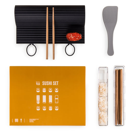 Sushi-Set mit Rollmatte Essstäbchen Reislöffel und zwei Gewürzbehältern auf einem orangen Untergrund.
