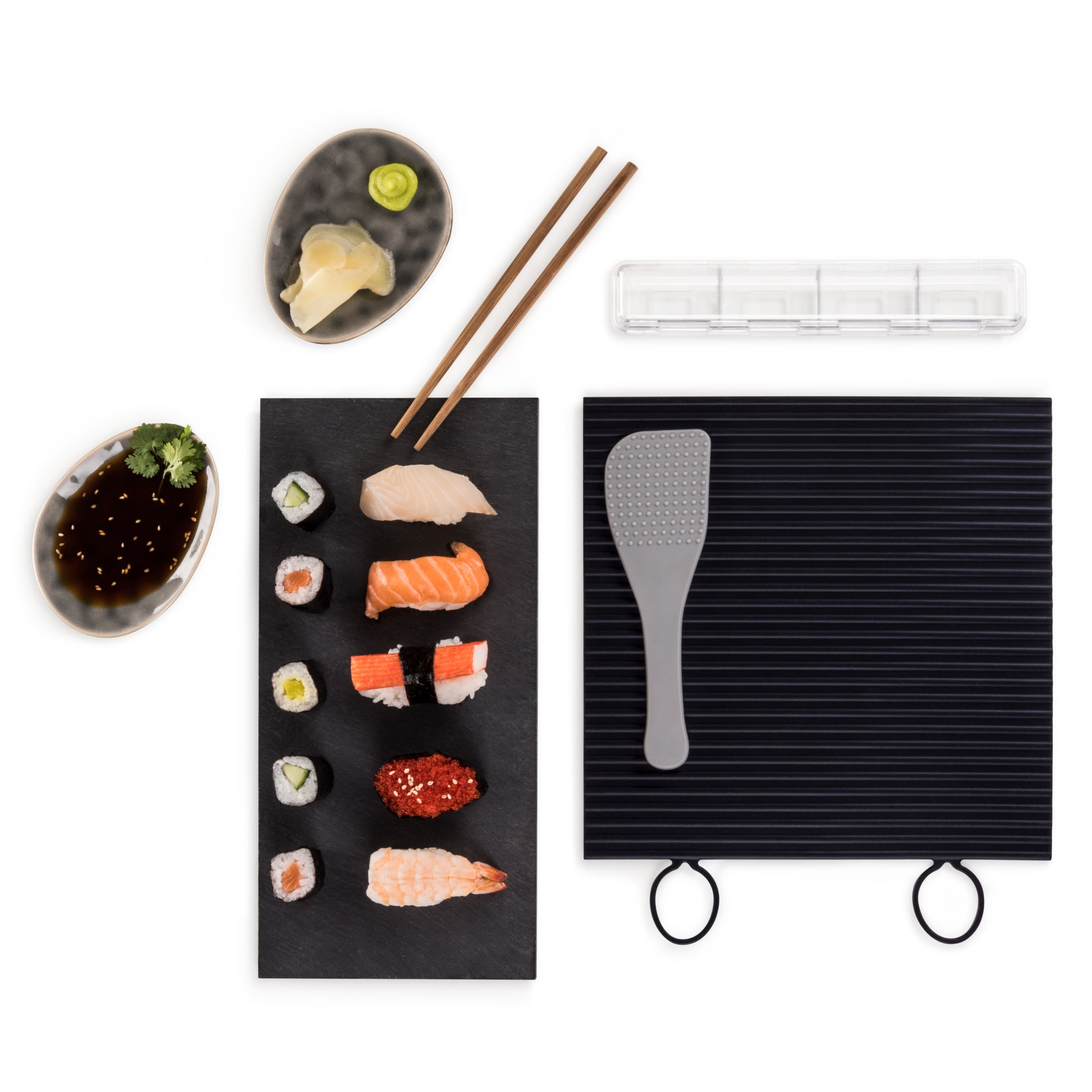 Zubereitetes Sushi auf einer schwarzen Platte mit Sojasauce Wasabi Ingwer Essstäbchen und Reislöffel.