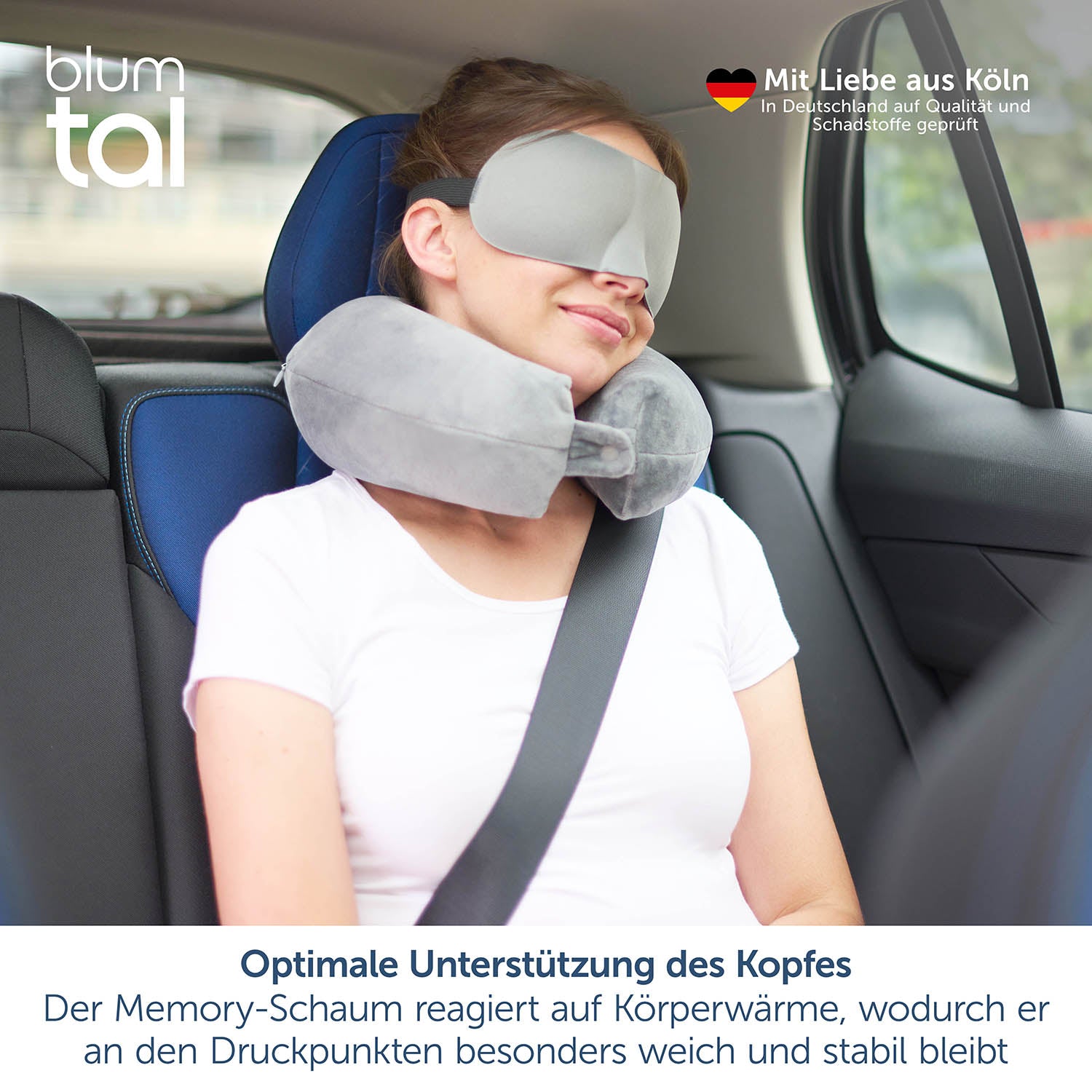 Das Bild zeigt eine junge Frau, die im Beifahrersitz eines Autos sitzt und ein graues Nackenkissen trägt. Sie hat auch eine Schlafmaske auf und lehnt entspannt zurück, wobei der Sicherheitsgurt angelegt ist. Oben links im Bild ist das blumtal-Logo zu sehen. Oben rechts steht "Mit Liebe aus Köln" und darunter "In Deutschland auf Qualität und Schadstoffe geprüft" neben einem deutschen Herz-Icon.