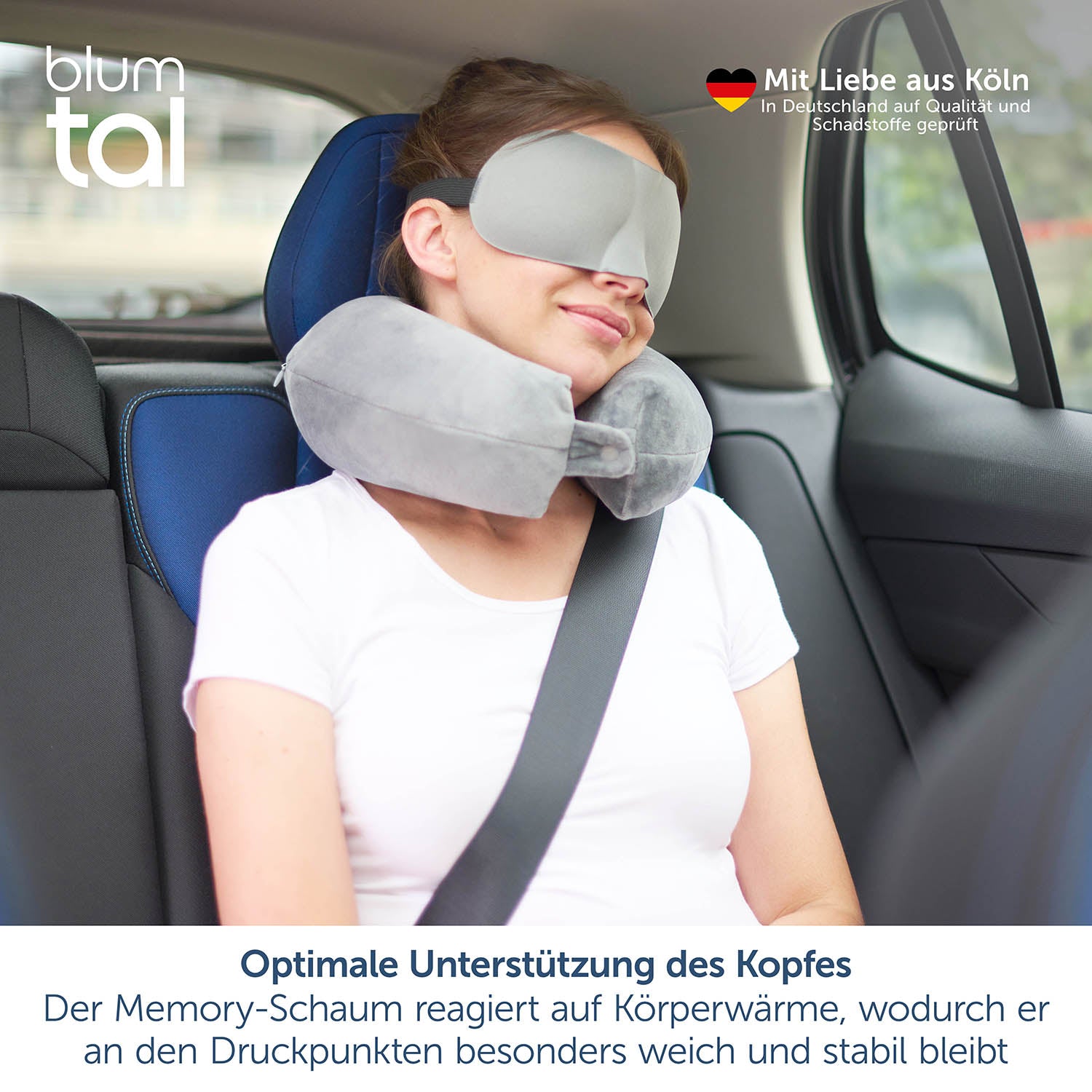 Das Bild zeigt eine junge Frau, die im Beifahrersitz eines Autos sitzt und ein graues Nackenkissen trägt. Sie hat auch eine Schlafmaske auf und lehnt entspannt zurück, wobei der Sicherheitsgurt angelegt ist. Oben links im Bild ist das blumtal-Logo zu sehen. Oben rechts steht &quot;Mit Liebe aus Köln&quot; und darunter &quot;In Deutschland auf Qualität und Schadstoffe geprüft&quot; neben einem deutschen Herz-Icon.