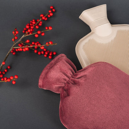 Rote Wärmeflasche neben Beerenstrauch und Tee-Set